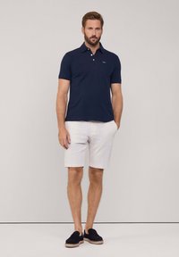 Polo shirt blu navy con maniche corte e tasca sul petto, abbinato a pantaloni corti bianchi e mocassini neri. Design semplice con una vestibilità classica.