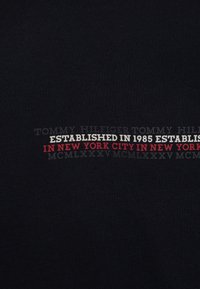Schwarzes Baumwollhemd mit Text in verschiedenen Schattierungen, einschließlich "TOMMY HILFIGER", "ESTABLISHED IN 1985" und "IN NEW YORK CITY", mit roten Akzentuierungen.