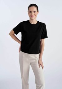 Czarna bawełniana koszulka z krótkim rękawem i okrągłym dekoltem, połączona z jasnymi beżowymi spodniami w kant. Gładka tekstura i dopasowany krój.