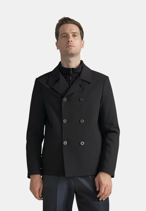 Giacca nera doppiopetto con ampi revers, dotata di bottoni metallici e una silhouette aderente. Il tessuto appare liscio e strutturato.