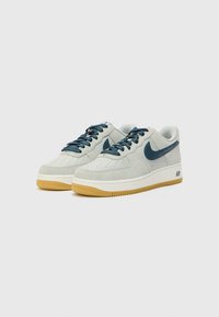 Suede and leather sneakers in light grey with dark blue accents and laces. Features rubber gum sole and perforations for ventilation.