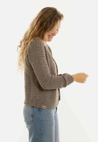 Beige gebreide cardigan met een textuurpatroon, geribbelde mouwen en een rechte snit. Gecombineerd met blauwe denim jeans.