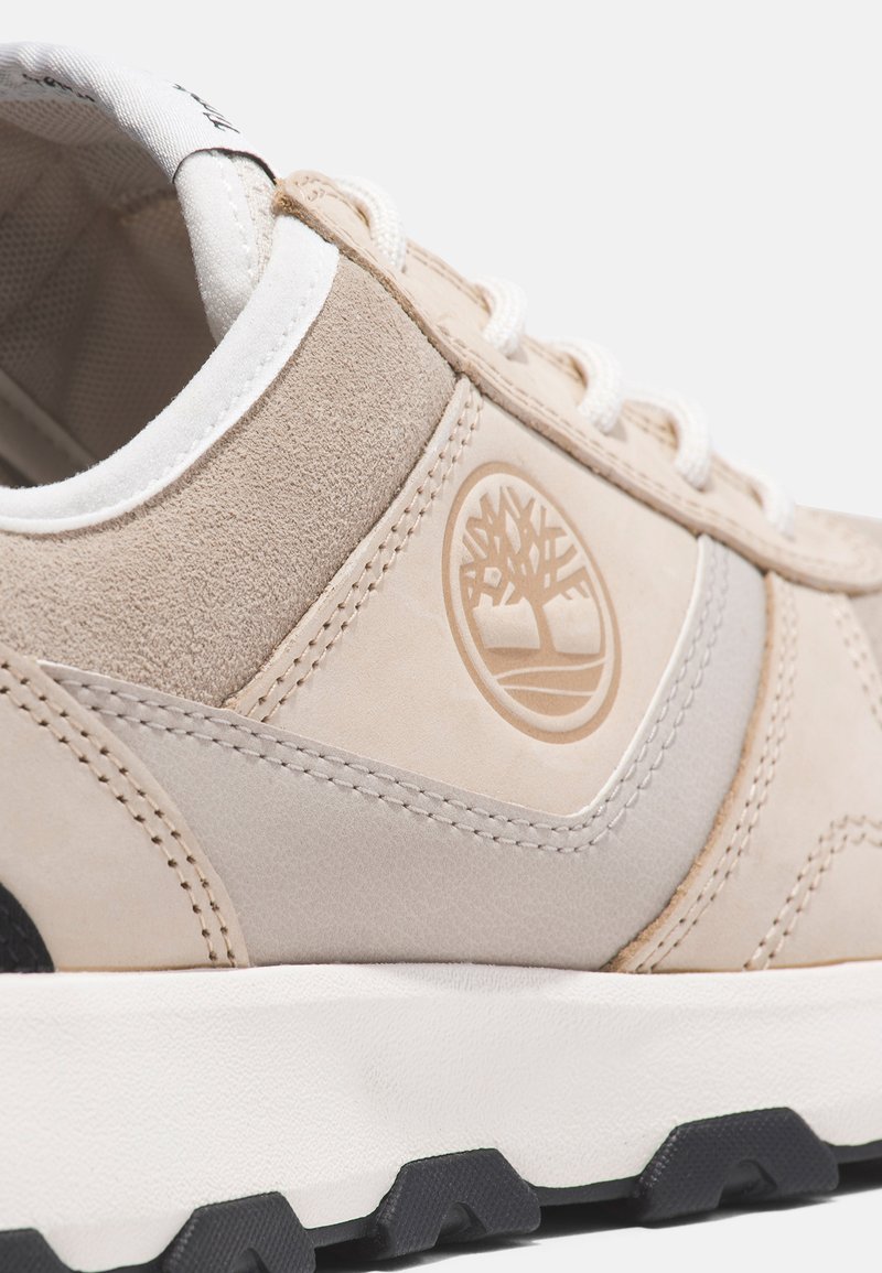 Beżowe zamszowe i skórzane sneakersy o teksturowanej powierzchni, z haftowanymi detalami, białymi sznurowadłami oraz naszywką z logo. Gumowa podeszwa z bieżnikiem.