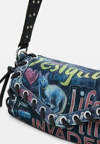 Jeans-Handtasche mit einem blauen Katzenmotiv und buntem Text. Schwarzer geflochtener Tragegurt mit metallischen Akzenten und Ösendetails.