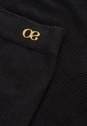 Zwarte geribde sokken met een zachte textuur, voorzien van een gouden "30" logo op de boord, die een minimalistisch ontwerp accentueren.