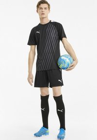 Sort atletisk fodbolduniform bestående af en kortærmet trøje med mørkegrå diagonale striber, sorte shorts, knæhøje sorte strømper og blå fodboldstøvler.
