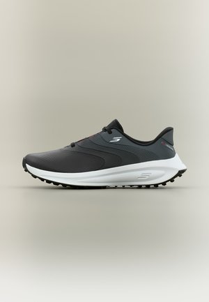 Schwarz-grauer Sportschuh mit weißer Sohle, strukturiertem Grip und seitlichem Logo, im Profil vor neutralem Hintergrund dargestellt.