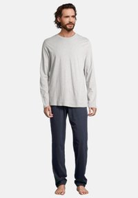 Grijze lange mouwen shirt gecombineerd met marineblauwe broek, beide gemaakt van zachte stof. Het shirt heeft een ronde halslijn; de broek is recht gesneden.