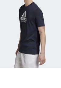 Námořnická modrá tričko s krátkým rukávem vyrobené z texturované tkaniny, s velkým bílým logem adidas přes hruď. Lehký a přiléhavý design.