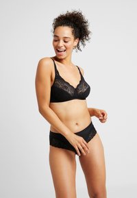Black lace bralette with soft cups and wide straps, paired with matching black brief featuring lace trim. Smooth fabric texture, no patterns.