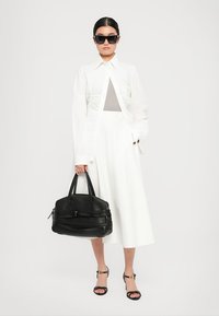 White shirt with pleated detail, white skirt, black leather bag, and black sunglasses. Sandals with ankle straps complete the look.