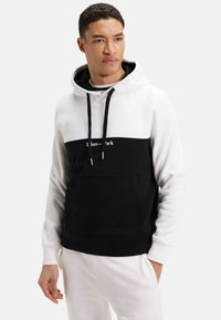 Sweat à capuche en blanc et noir. Caractéristiques : une poche avant, un cordon de serrage et un logo au niveau de la poitrine. Fabriqué en tissu doux.