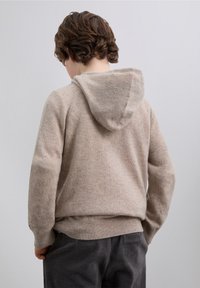 Hellbeiger, strukturierter Hoodie mit Kordelzugkapuze, gerippten Bündchen und Saum. Getragen mit dunkelgrauer Cordhose.