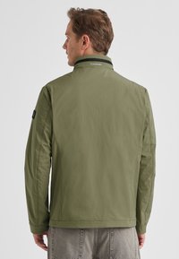 Olive green jacket with a high collar, made from lightweight material. Features subtle stitching and a logo on the back neckline.
