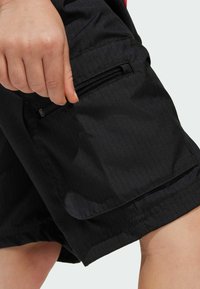 Černé kraťasy vyrobené z lehké tkaniny, s kapsou na zip a s texturovaným povrchem s jemnými vertikálními pruhy.