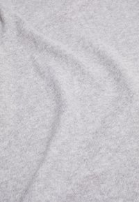 Tissu tricoté doux gris clair avec une texture subtile et de légers plis créant des ombres douces à la surface.