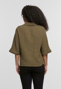 Top verde oliva, con texture, dalla vestibilità morbida, maniche piegate e colletto, abbinato a jeans skinny neri.