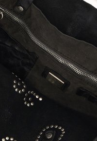 Interno di una borsa in tessuto nero con cerniera argentata, accessori in metallo e borchie decorative rotonde disposte in un motivo curvo.