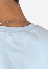 Světle modré bavlněné tričko s kulatým výstřihem, na zadní straně se bílým vyšitým diamantovým logem. Hladká textura, příležitostný design.