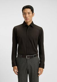 Donkerbruine overhemd met lange mouwen, een knoopsluiting aan de voorkant, klassieke kraag en zwarte knopen, gecombineerd met grijze geblokte broek en een bruine riem.