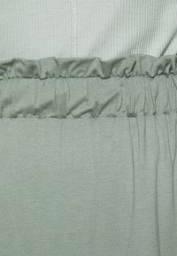 Vaaleanvihreä ribattu kangas, jossa on elastinen vyötärö, ja ylhäällä on röyhelömäinen rakenne sekä alhaalla sileä pinta.