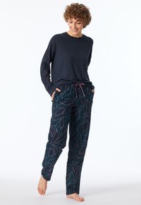 Marineblauw langwerpig shirt met ronde hals; gemusterde joggers met trekkoord met teal en paarse bladeren op een donkere achtergrond.