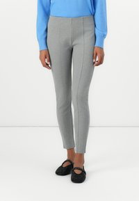 Grijze leggings met een strakke pasvorm, voorzien van zijnaadstiksels, gecombineerd met zwarte versierde flats en een lichtblauw langemouwenshirt.