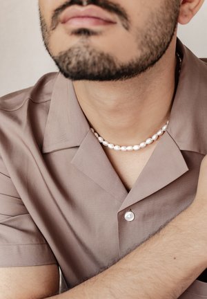 Brown collared shirt made of smooth fabric with a buttoned front, paired with a white pearl necklace featuring oval beads.