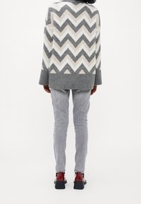 Grau und weiß gestreifter Pullover mit lockerer Passform, kombiniert mit hellgrauen Jeans und roten glänzenden Schuhen, von hinten betrachtet.