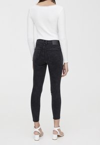 Jeans skinny de cintura alta en color negro con una textura desgastada, que cuentan con bolsillos traseros y un diseño sencillo. Combinados con una camiseta de manga larga blanca.