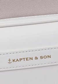 Weiße synthetische Materialien mit einer strukturierten Oberfläche, die mit goldener "KAPTEN & SON"-Markierung und weißem Stoff entlang der Kante versehen sind.