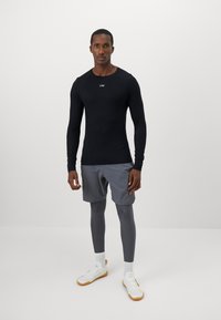 Camisa desportiva de manga longa preta, calções cinzentos, leggings cinzentos e ténis brancos com solas laranja. Design simples, sem padrões visíveis.