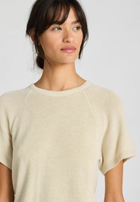Cream-colored short-sleeve knit top with a round neckline, ribbed accents, and a soft texture. Features raglan sleeves for a relaxed fit.