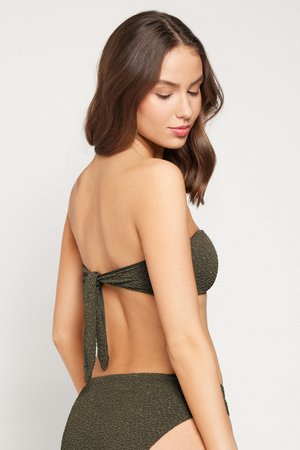 Frau mit schulterlangem braunem Haar, die einen strukturierten dunkelgrünen trägerlosen Bikini trägt, seitlich gedreht mit geschlossenen Augen vor einem einfarbigen Hintergrund.