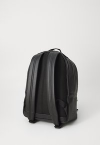 Zaino nero con esterno in pelle liscia e retro in rete testurizzata, dotato di due spallacci imbottiti e una maniglia superiore per il trasporto.