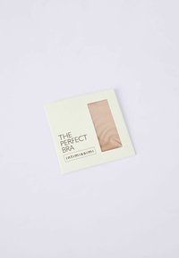 Indpakket bh med et gennemsigtigt vindue. Lys beige stof, glat tekstur og minimalistisk hvid emballage med sort tekst.
