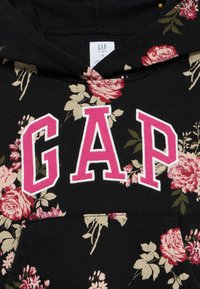 Μαύρο φούτερ με κουκούλα και ανθισμένο σχέδιο σε αποχρώσεις ροζ και μπεζ. Λογότυπο "GAP" σε έντονο ροζ στο στήθος. Υλικό από μείγμα βαμβακιού.