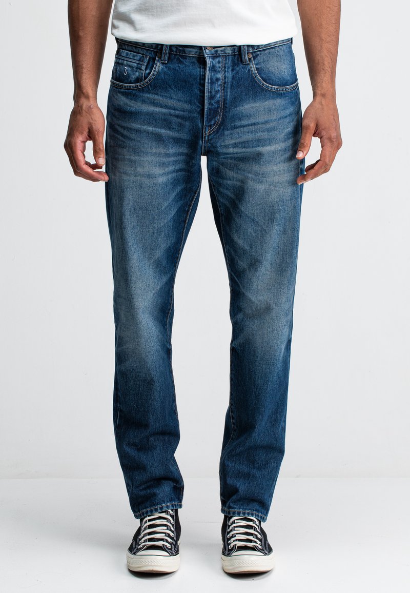 Jeans aus Denim in einem mittleren Blauton mit geradem Bein. Mit fünf Taschen, leichter Ausbleichung und Reißverschluss. Kombiniert mit schwarzen Sneakers.
