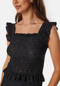 Top in pizzo nero a occhio di pernice, scollo quadrato, maniche corte a volant, orlo a volant stratificato, tessuto testurizzato con motivi aperti.