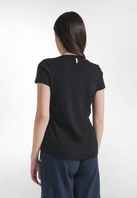 Camiseta de algodón negro con mangas cortas y cuello redondo, con una pequeña etiqueta de la marca en la parte trasera. Textura suave, ajuste relajado.