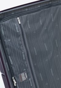 Interno della valigia viola con scomparto a rete con zip; presenta un tessuto grigio con motivo aereo e etichette del marchio, texture liscia.