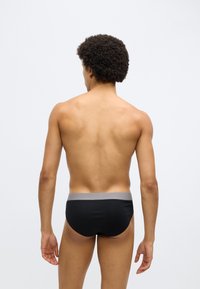 Fekete fürdőnadrág szürke elasztikus derékrésszel. Egyszerű kialakítás, sima textúrával és testhez simuló formával. A termék hátulnézete.