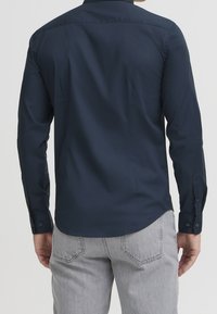 Marineblauw overhemd met lange mouwen, recht afgewerkte zoom en puntige kraag. Voorzien van knoopsluiting bij de manchet en gemaakt van een soepele, lichte stof.