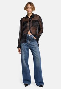Schwarze, durchsichtige Knopfleiste mit zwei Brusttaschen, kombiniert mit hellblauen Jeans aus Denim mit Nietenakzenten und weitem Bein.