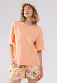 Lys orange bomulds t-shirt med korte ærmer og rund hals, parret med pink shorts med citrusfrugt mønstre og grønne blade.