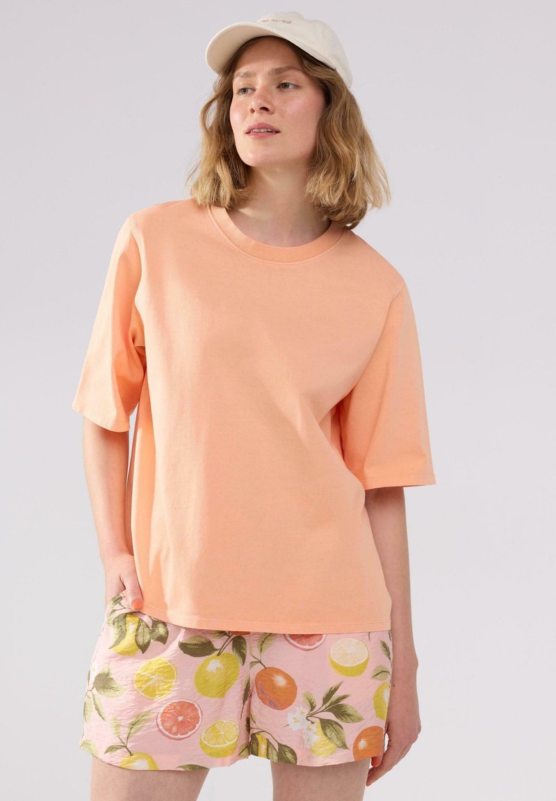 Lys orange bomulds t-shirt med korte ærmer og rund hals, parret med pink shorts med citrusfrugt mønstre og grønne blade.