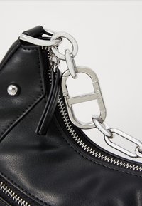 Black faux leather bag with silver hardware, featuring a chain strap, zipper detail, and a small black leather tag attached.
