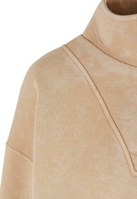 Beige pulóver magas gallérral, puha tapintással és finom tónusbeli eltérésekkel. Az nyakrésznél varrott díszítések találhatók.