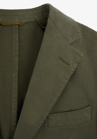 Blazer verde oliva con solapa de muesca, bolsillo de ojal en el pecho y costuras visibles en el cuello y los bordes del bolsillo.