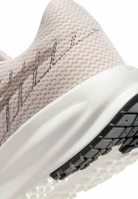 Gros plan d’un talon de chaussure de sport beige en mesh avec une semelle intermédiaire blanche amortie et une semelle extérieure en caoutchouc noir texturée.